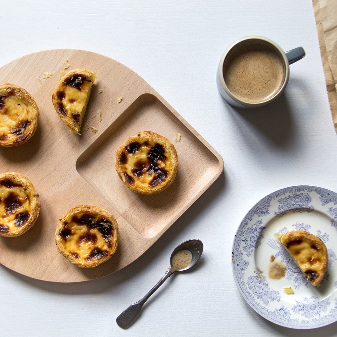 Wooden tray with golden pastries, blue floral plate, and a gray mug with coffee on a white background.