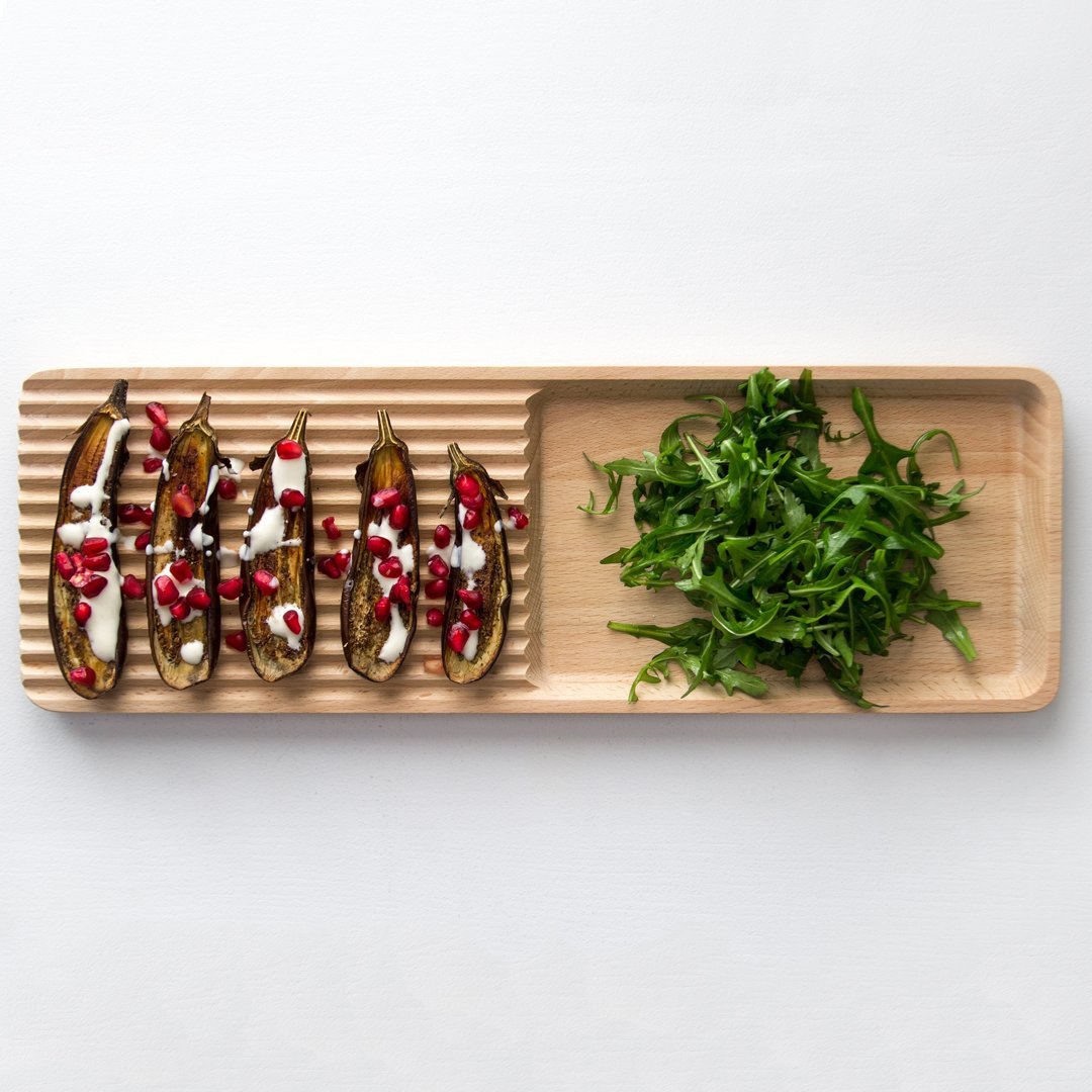 Bamboo serving platter featuring earthy tones with striped and smooth patterns, topped with vibrant greens and colorful toppings.