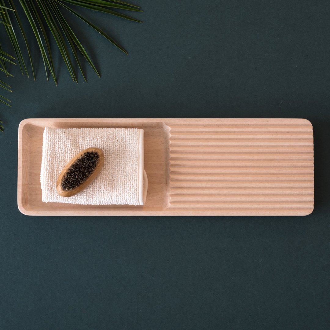 Light wooden rectangular tray with ridges, featuring a white towel and black caviar, set against a dark green surface.