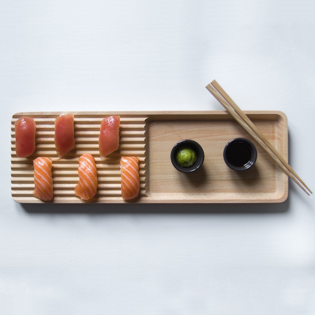 Wooden sushi platter featuring alternating salmon and tuna, with vibrant green lime and sleek black sauce dishes.