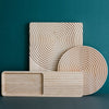 Natural wood serving trays featuring spiral and linear patterns in light beige tones against a teal background.