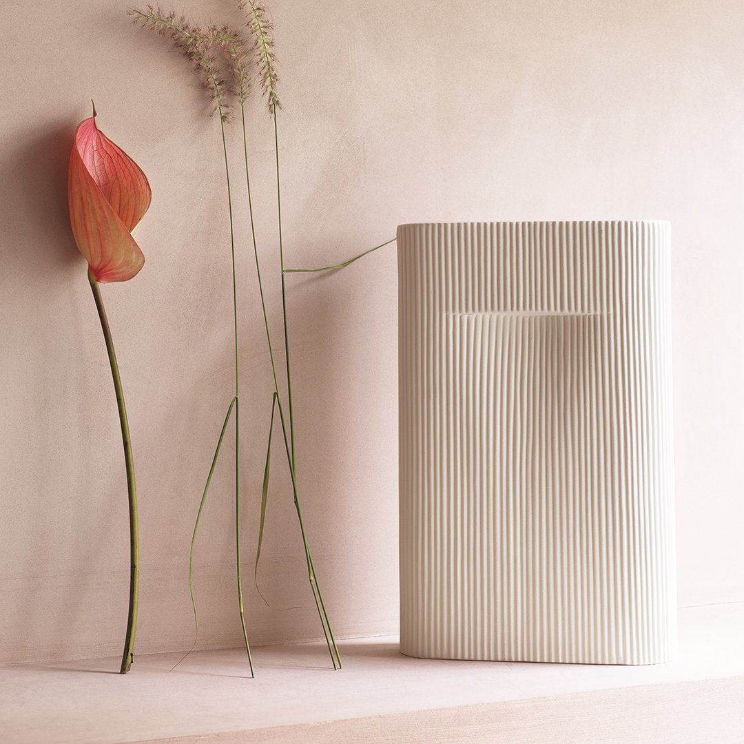 Textured cream vase with vertical stripes, complemented by soft pink flower and neutral background.