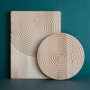 Natural wood serving board and plate with concentric circle patterns, showcasing light beige tones against a teal backdrop.