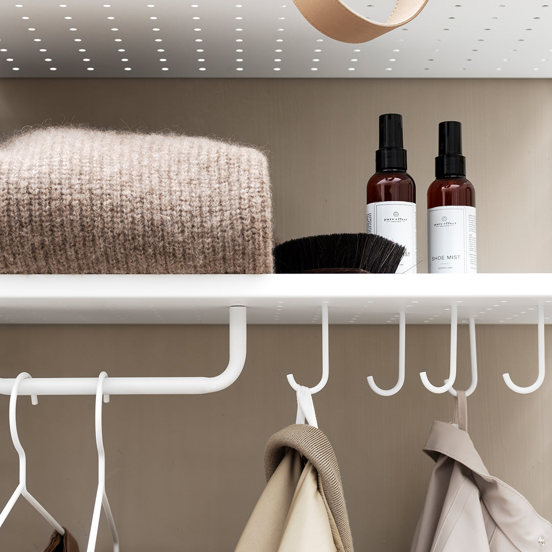 Soft beige sweater, black hair comb, and brown spray bottles on a white shelf against a neutral wall. Modern and minimalist.