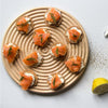 "Round wooden platter with circular grooves showcasing vibrant orange salmon on cream cheese spread, garnished with dill."